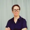 A photo of Jenny Read with her arms crossed standing against a light blue curtain background.