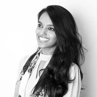 A black-and-white photo of Nivashinee Krishnakumar smiling in front of a white wall.