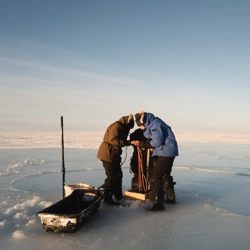 Photo of a team of people dressed in warm winter gear working on a water pump on an ice field in Canada