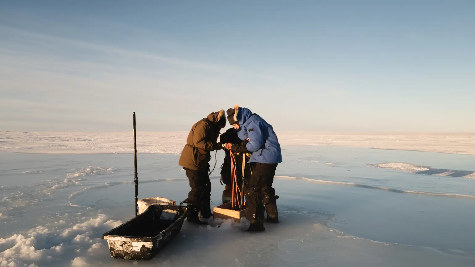 Photo of a team of people dressed in warm winter gear working on a water pump on an ice field in Canada
