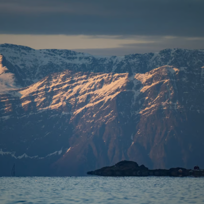 Snow-capped mountains at sunset with a small rocky island in the foreground
