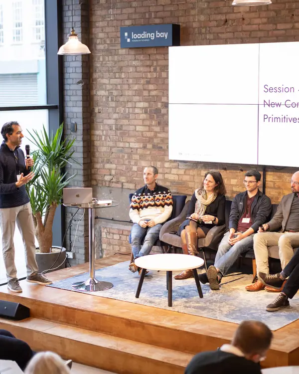 Four people sitting in a panel with a host speaking at an event