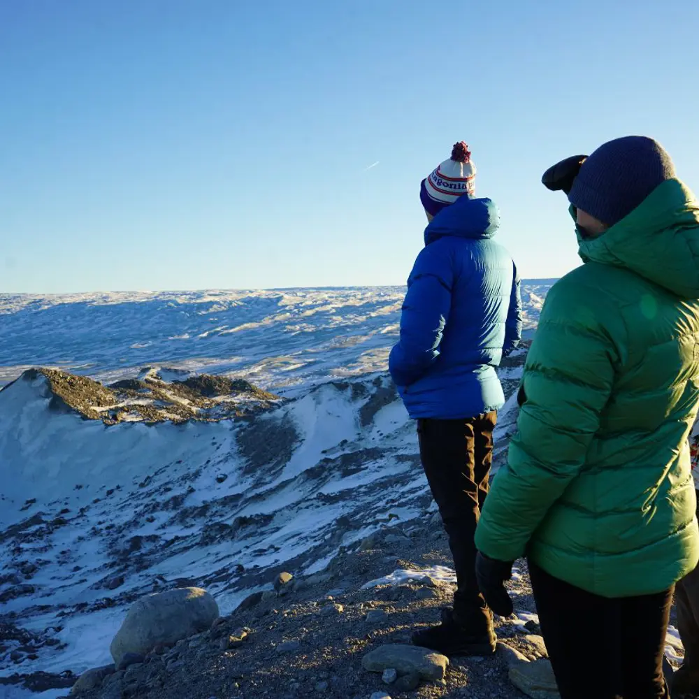 A photograph of two people in warm jackets looking out on a snowy landscape
