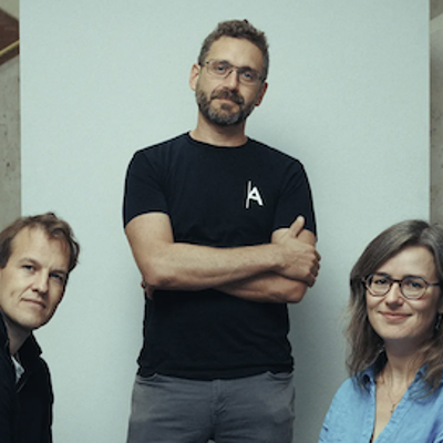 A photo of Matt Clifford, Ilan Gur and Angie Burnett looking at the camera. Matt and Angie are sat down and Ilan is standing.