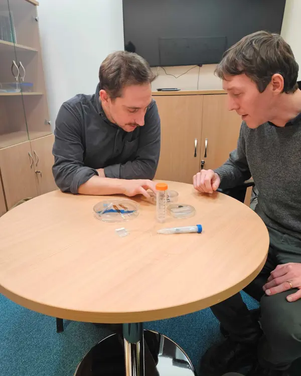 A photo of Jacques and another person looking at items on a table.