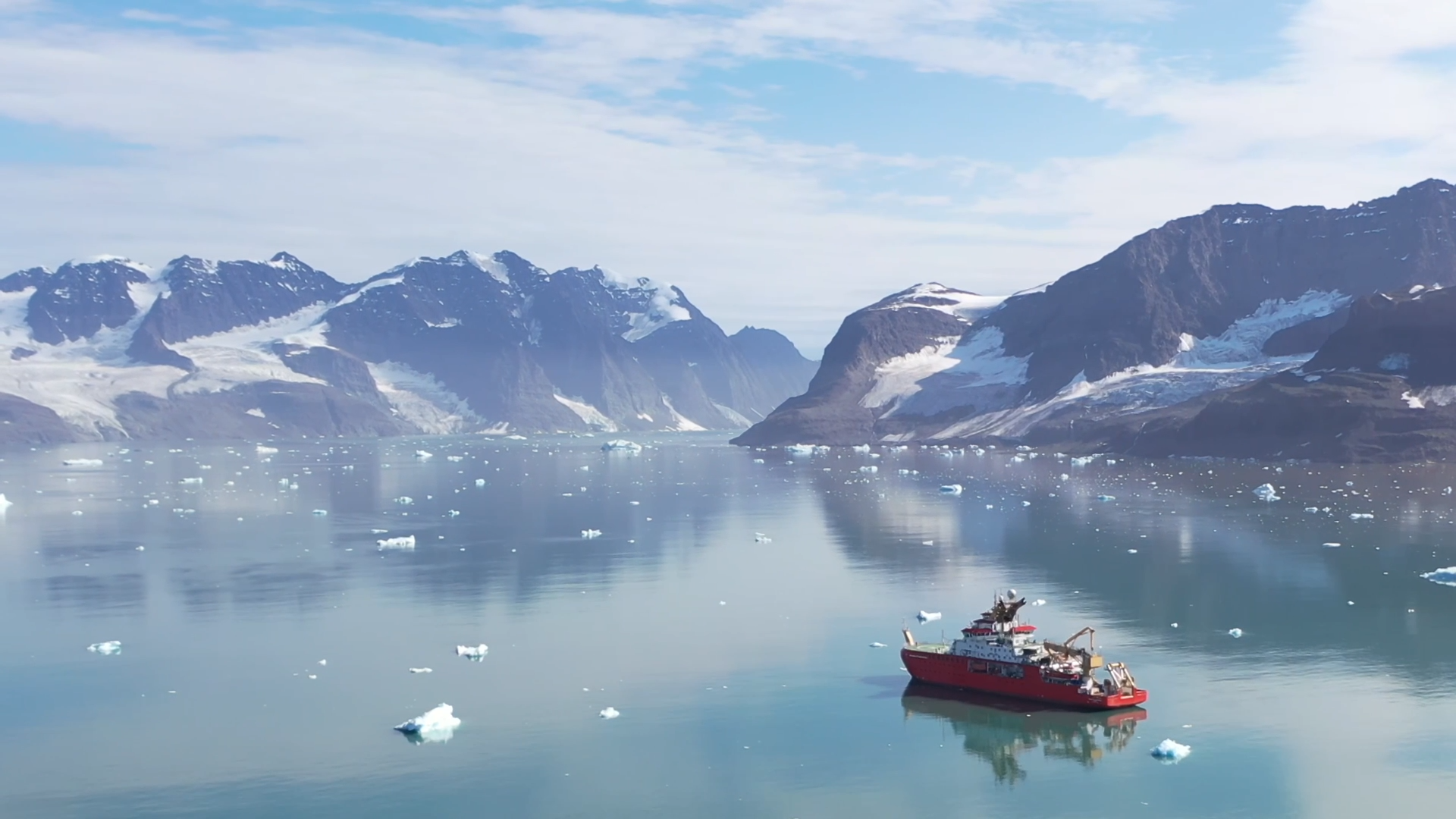 A red boat floating in the Arctic Ocean with mountains in the background