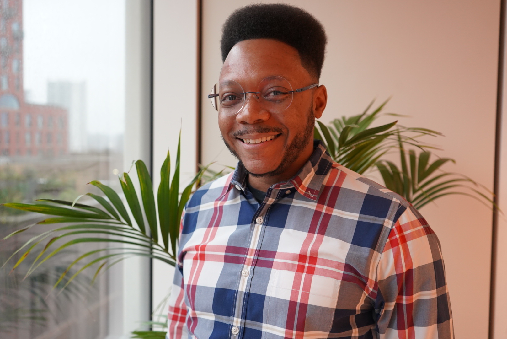 Headshot of David Lewis standing in front of a large window with a plant behind him