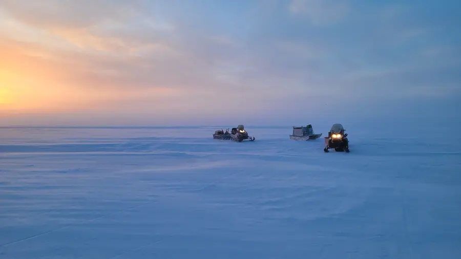Three snow mobiles sitting on an ice plain with a sunset in the background