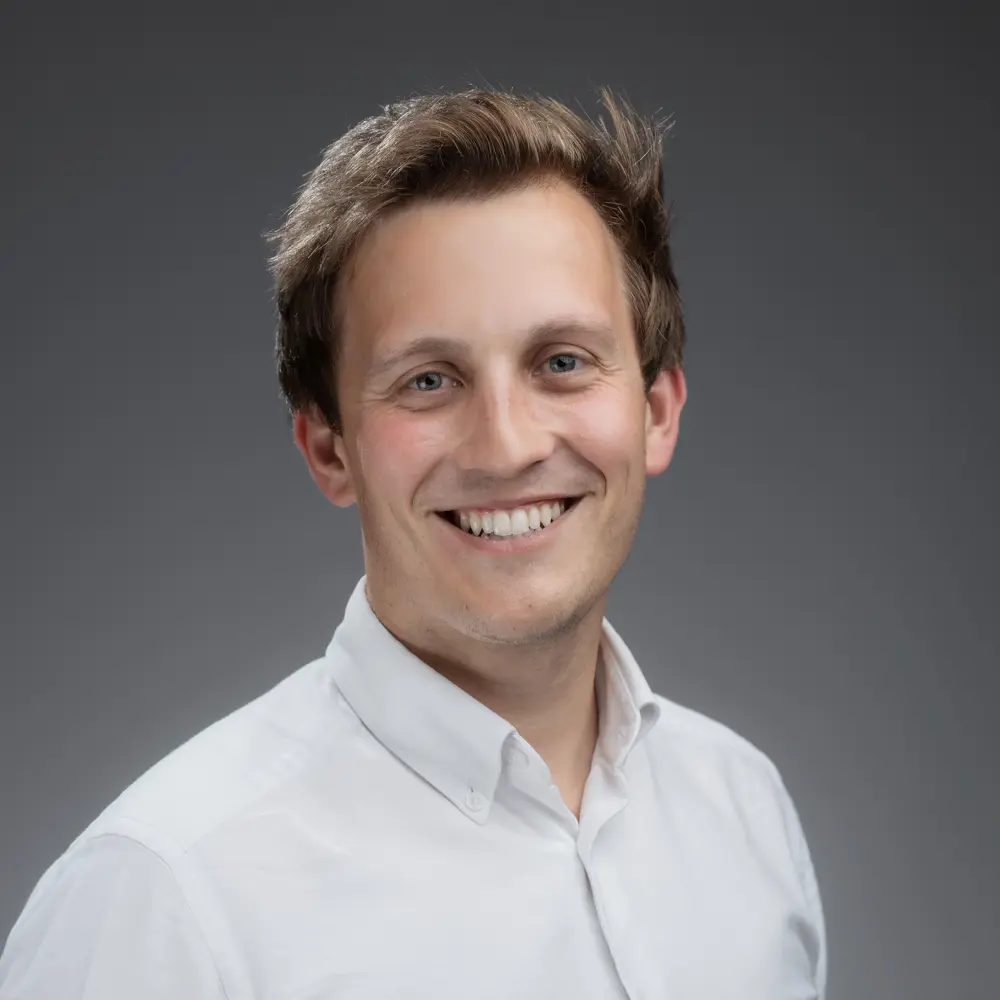 A photo of David Stringer smiling in front of a grey wall.