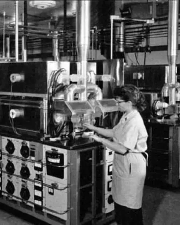 A black and white photo of a woman working in a factory with other people in the background